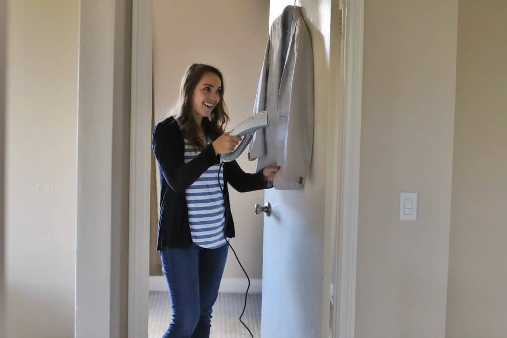 A woman steam cleans a suit jacket with a smile on her face