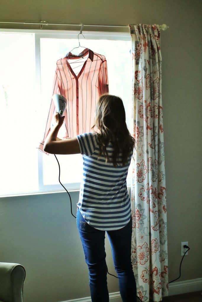 A woman uses a portable steamer on a pink shirt